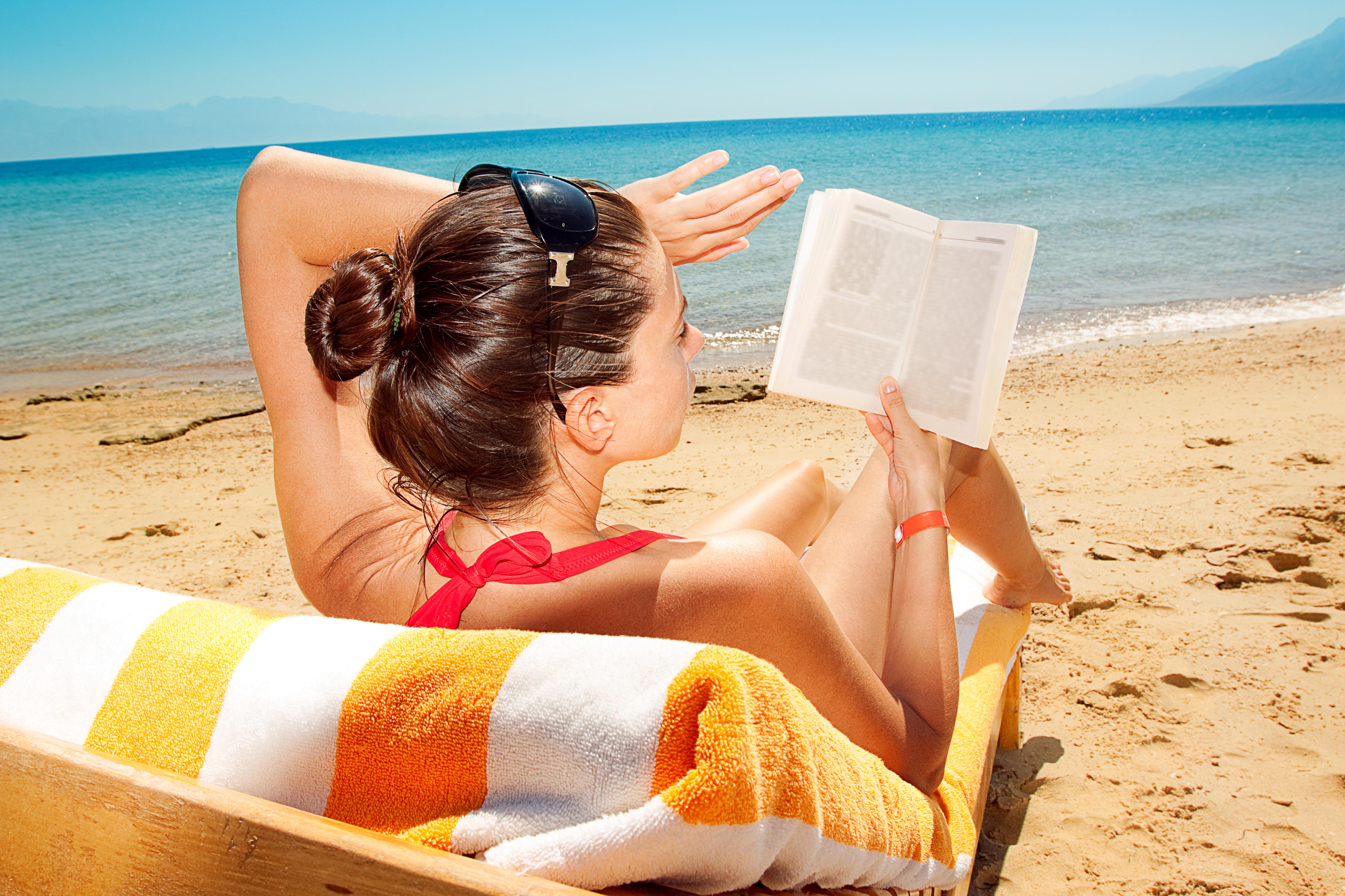 Бюджетно отдохнуть летом. Загорать на пляже. Девушка на пляже с книжкой. Загорать летом.